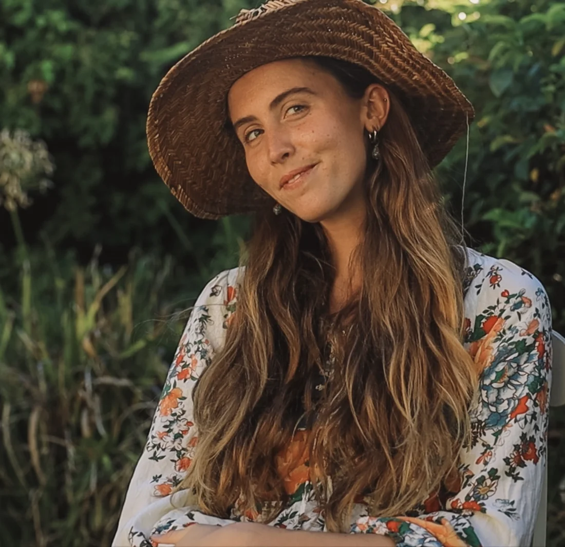Jess Holing, smiling, wearing a woven sun hat in a garden.