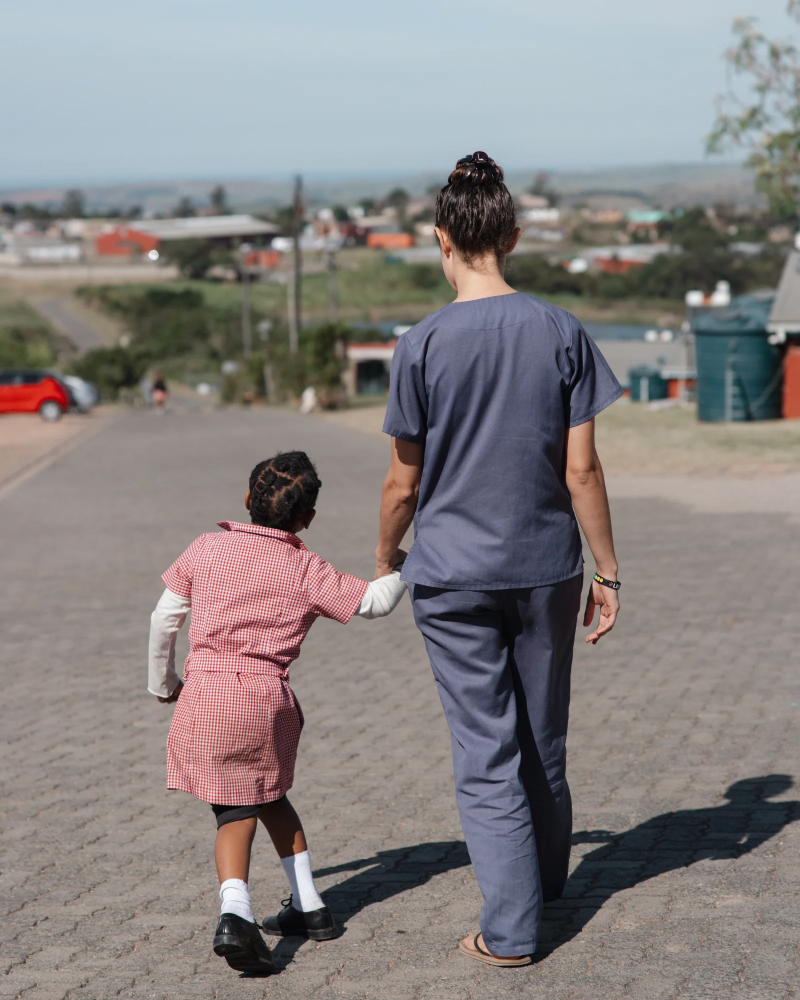 Amanda, in school uniform, walks hand in hand with a caregiver.