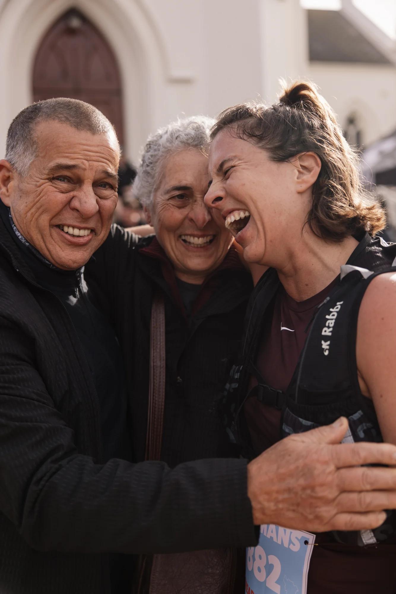Three trail runners laugh together at the finish line.