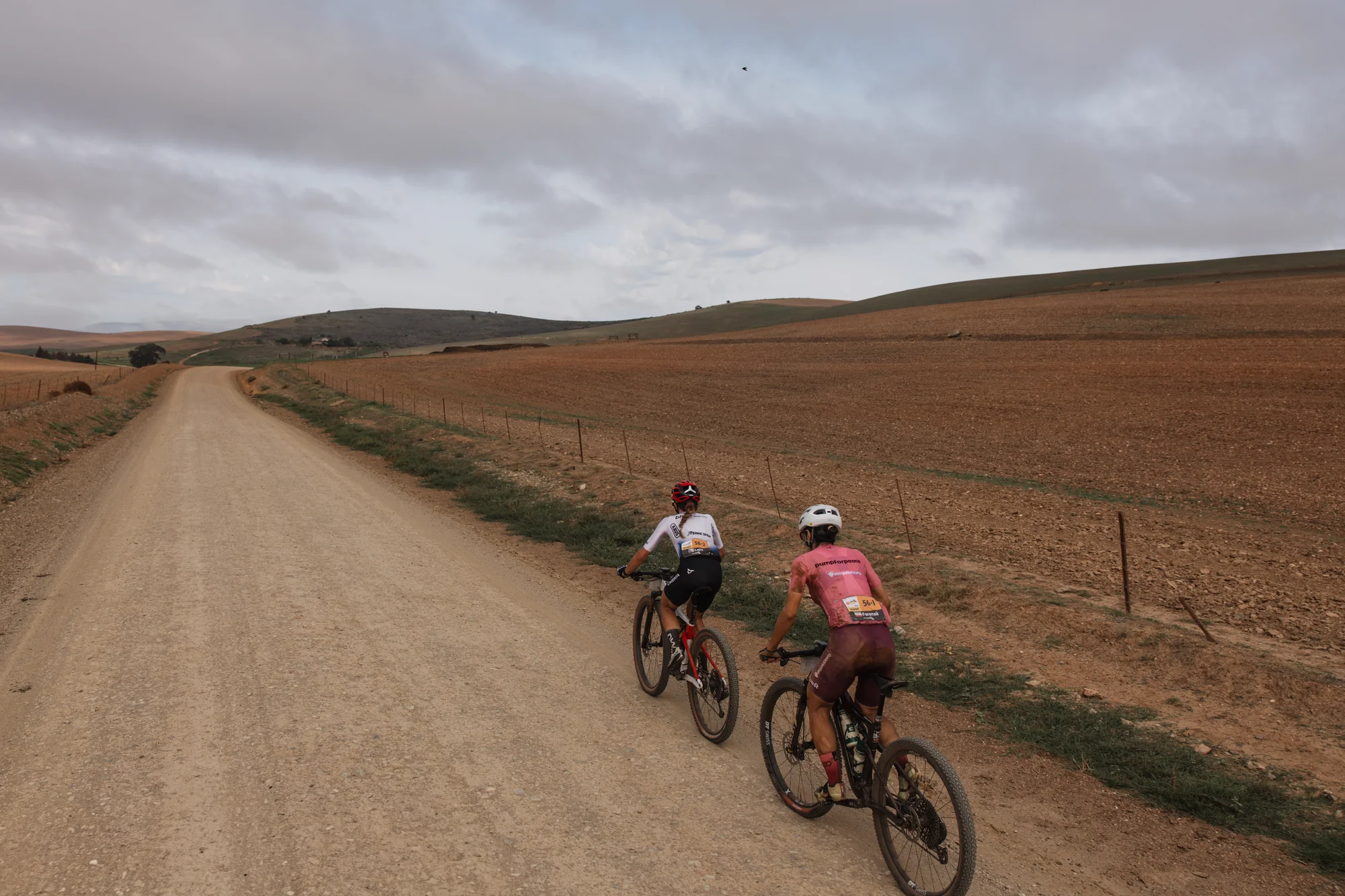 A wide gravel road, riders in the distance
