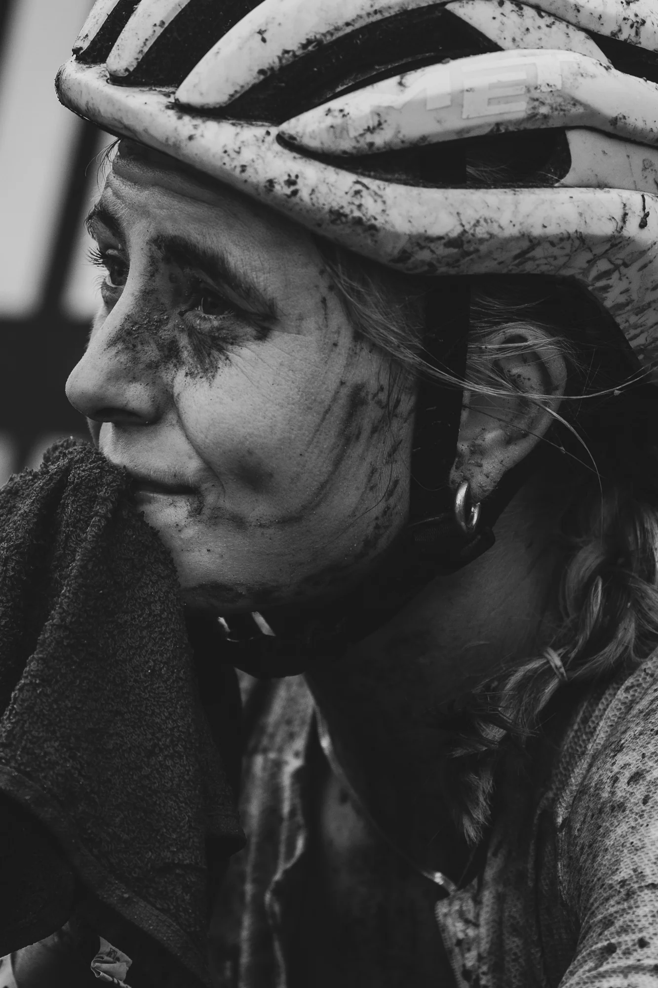 A mud-splattered mountain biker in a helmet, mid-race, in black and white.