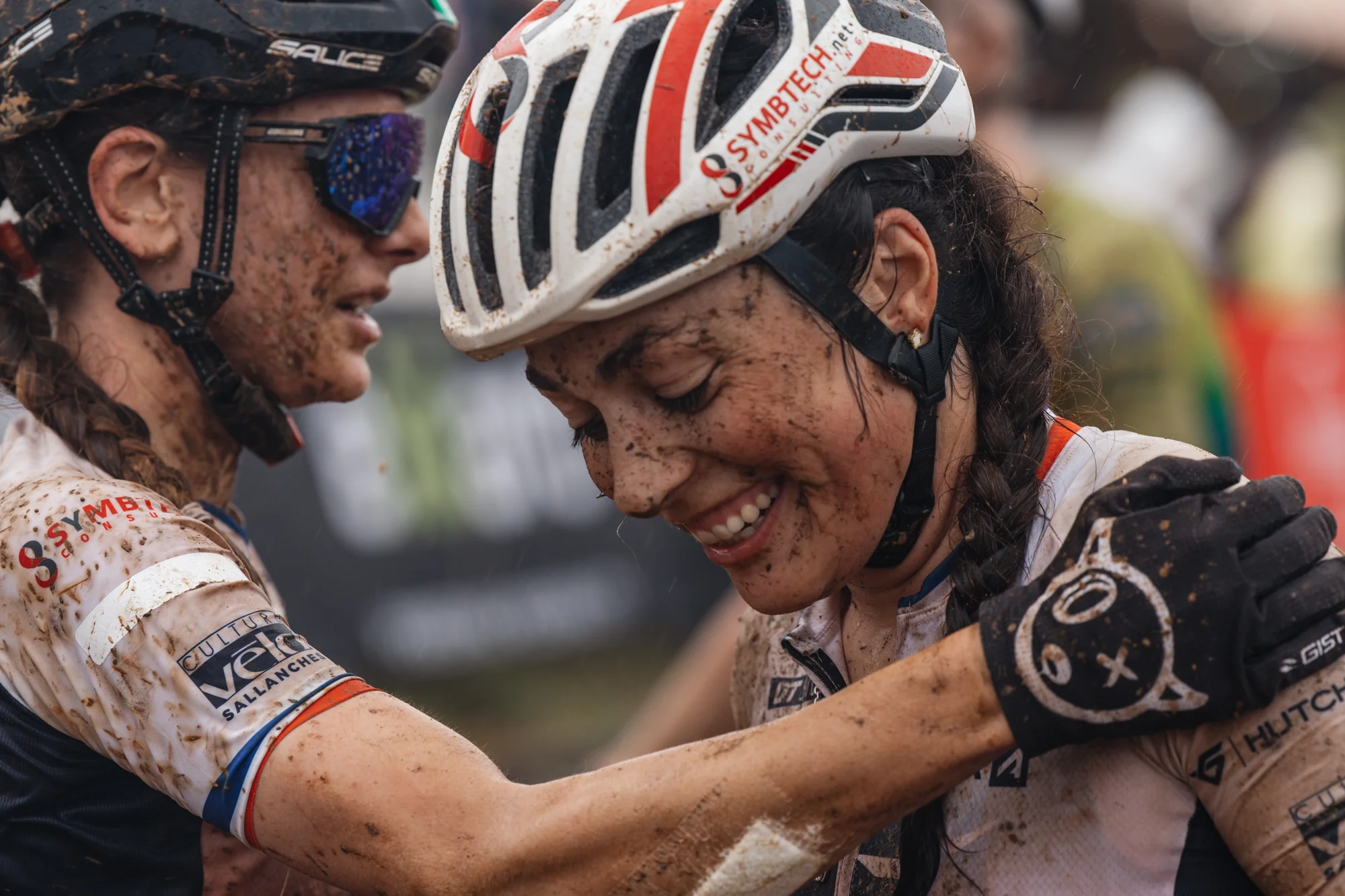 Two riders embracing, arm around each other, muddy