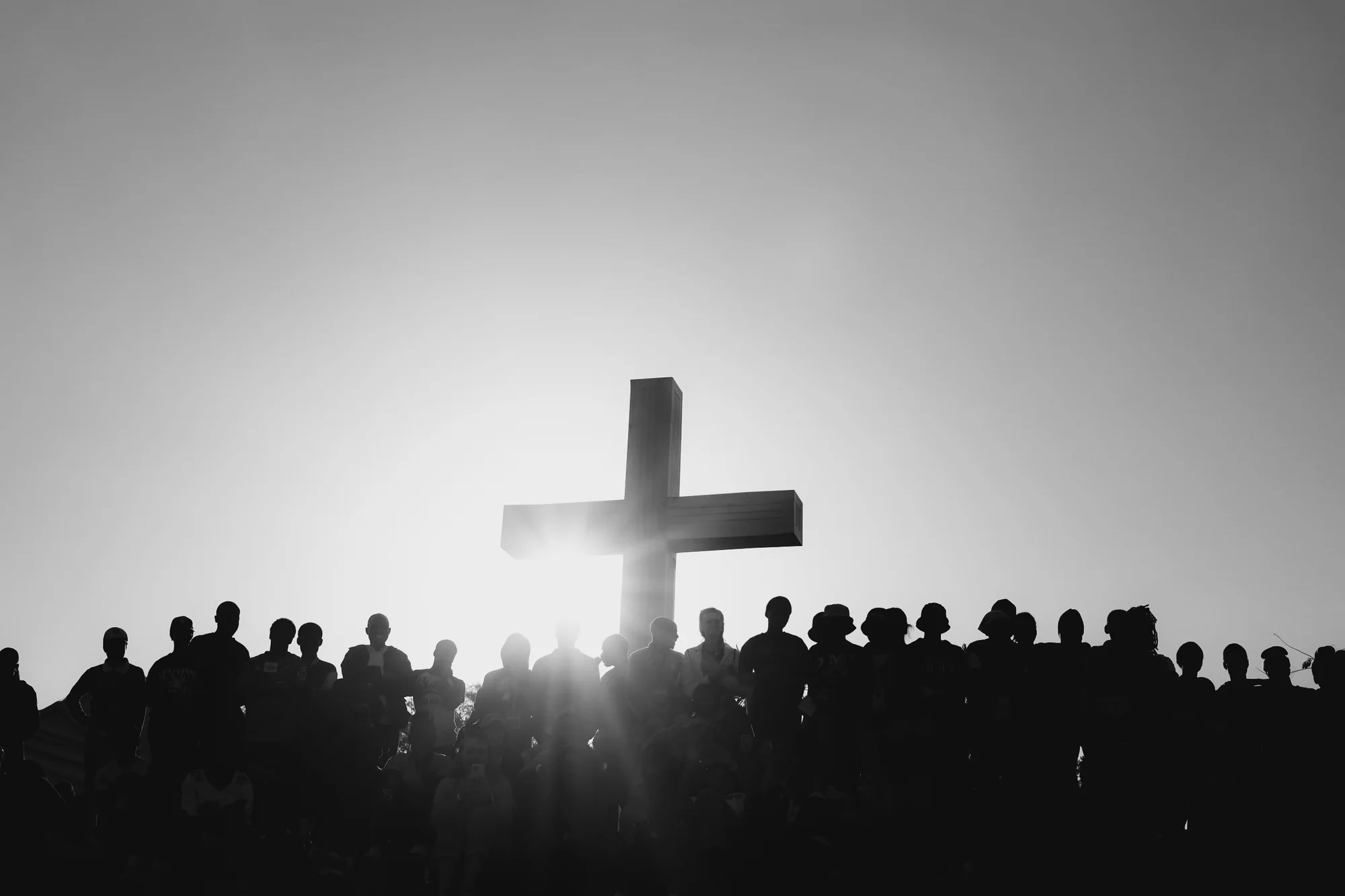 A cross silhouetted against the sky, a gathered crowd, black and white