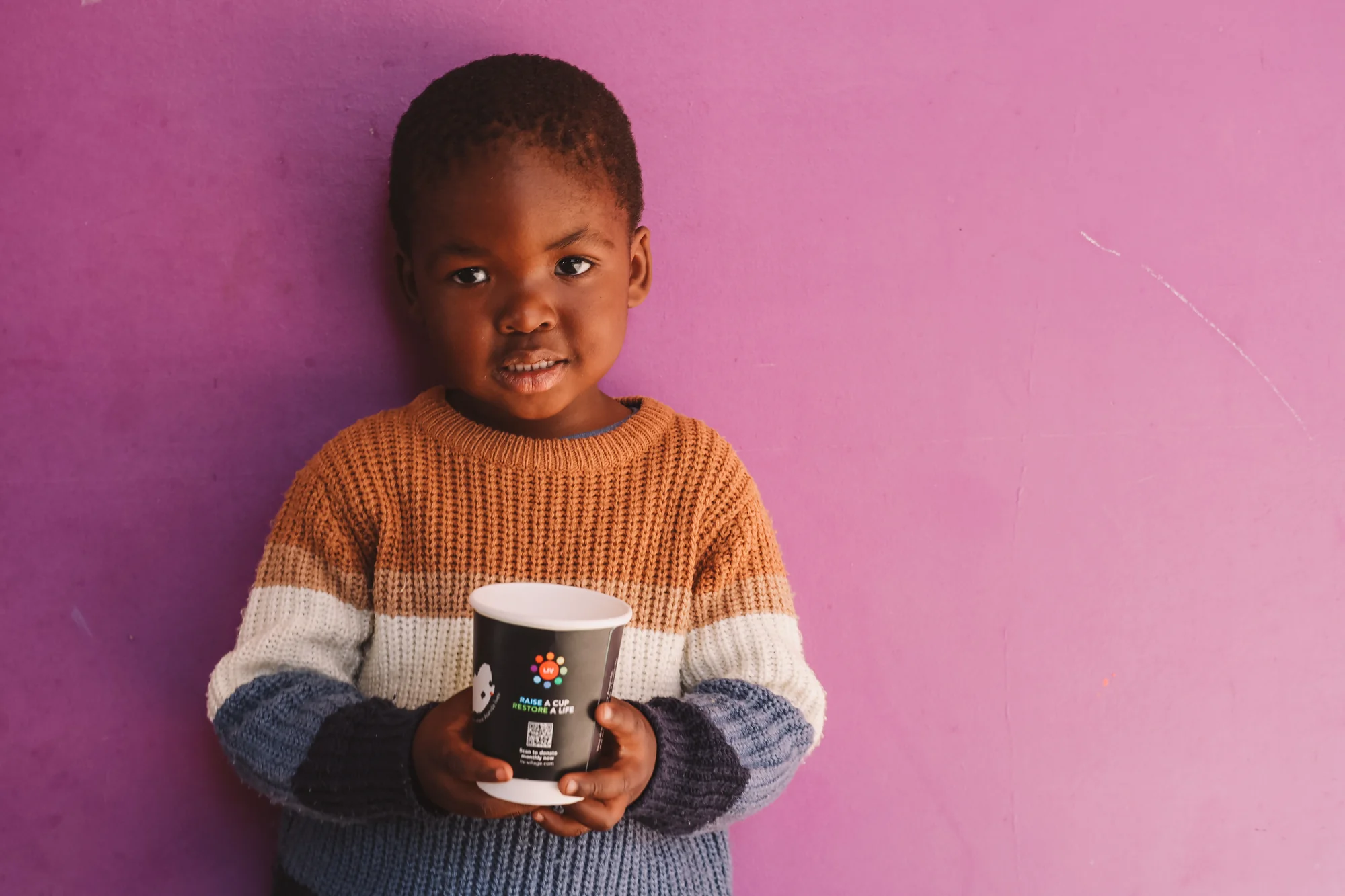 A child's portrait, holding a mug, against a pink wall