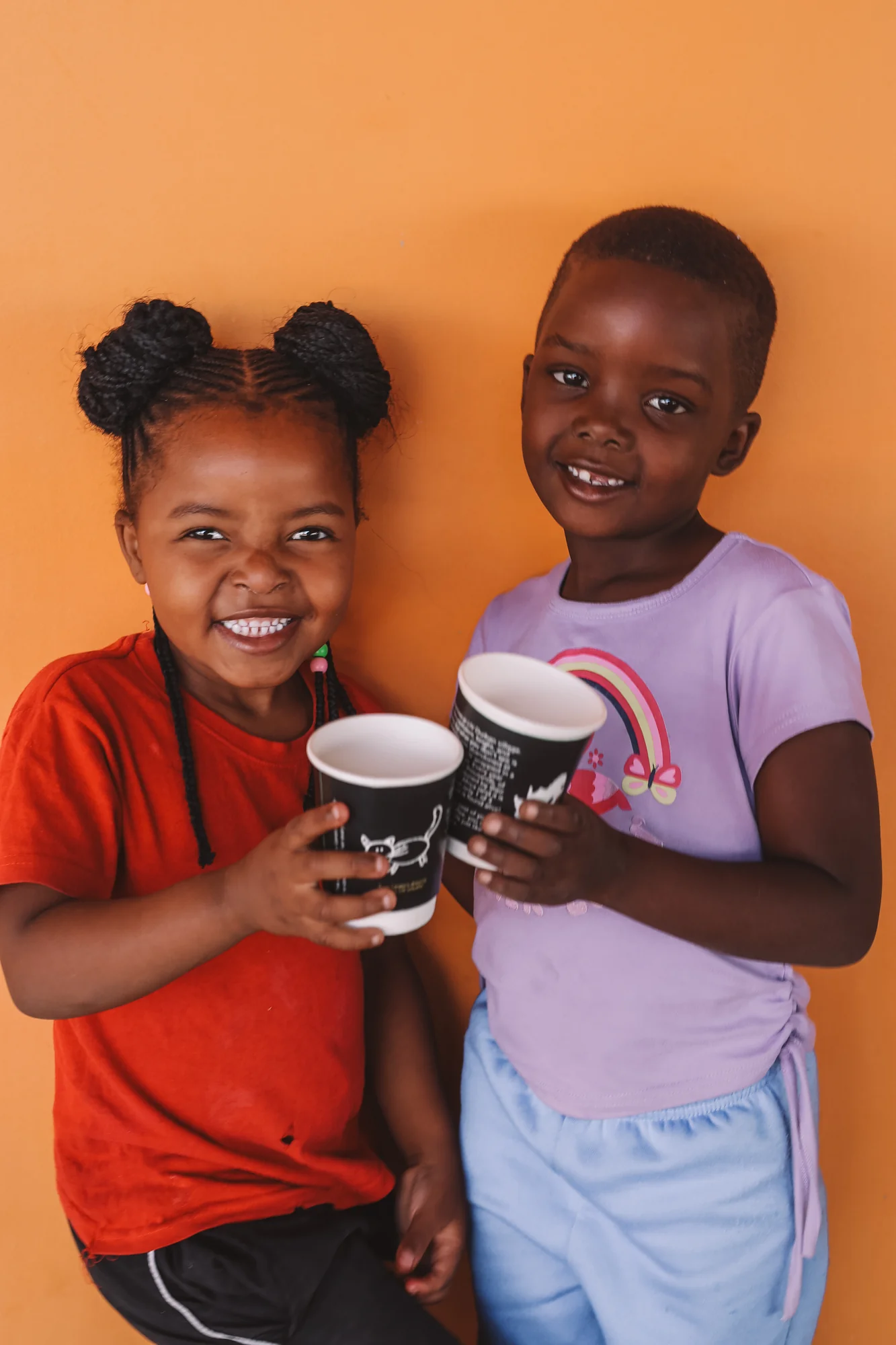 Two children, mugs raised, against an orange wall