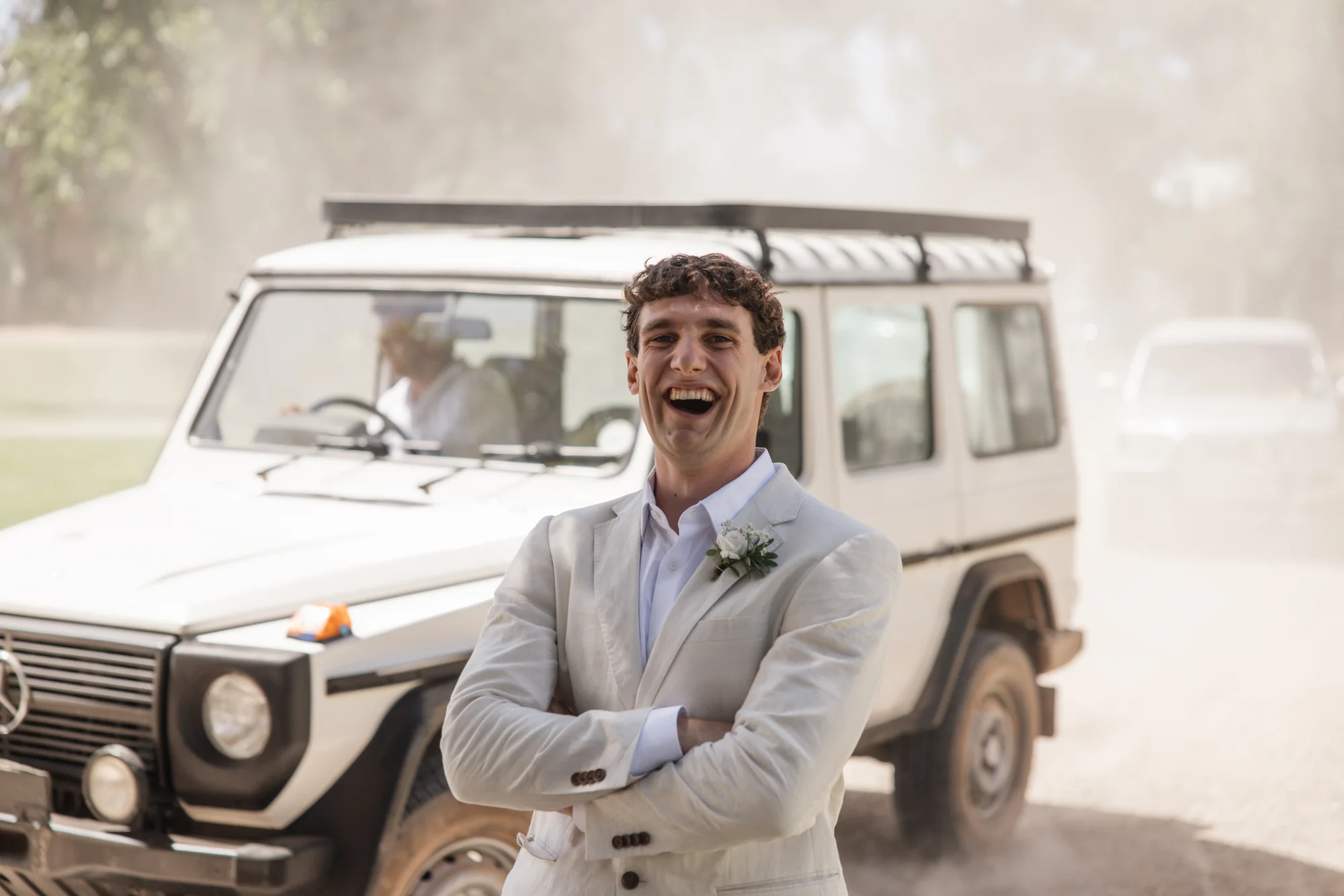 The groom laughing in the car on a dusty road