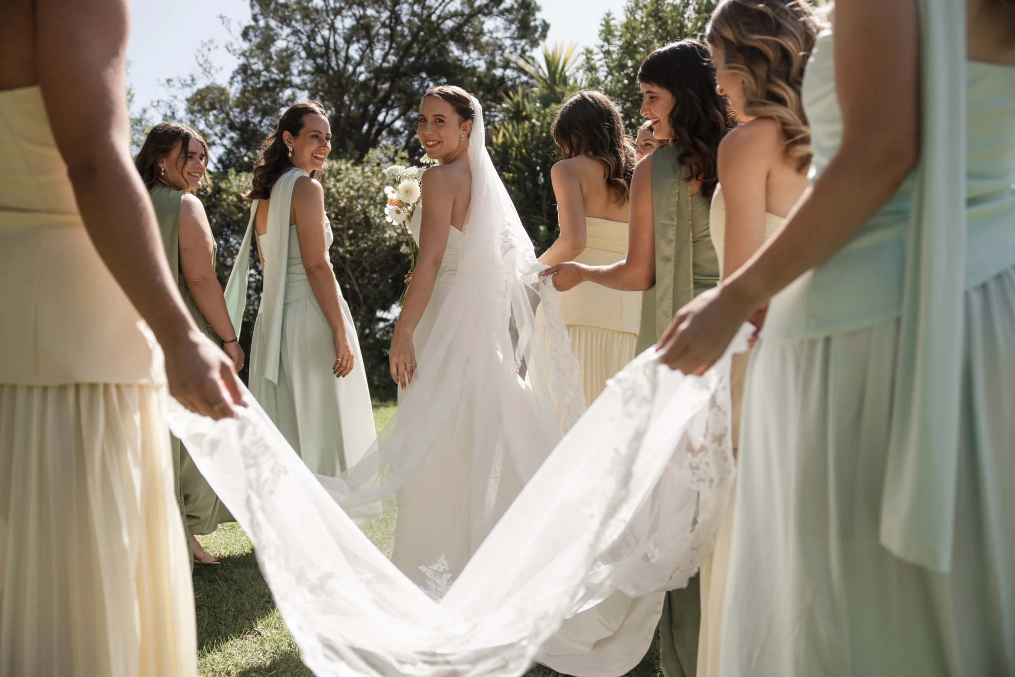 A bride glances back over her shoulder as bridesmaids hold her veil.