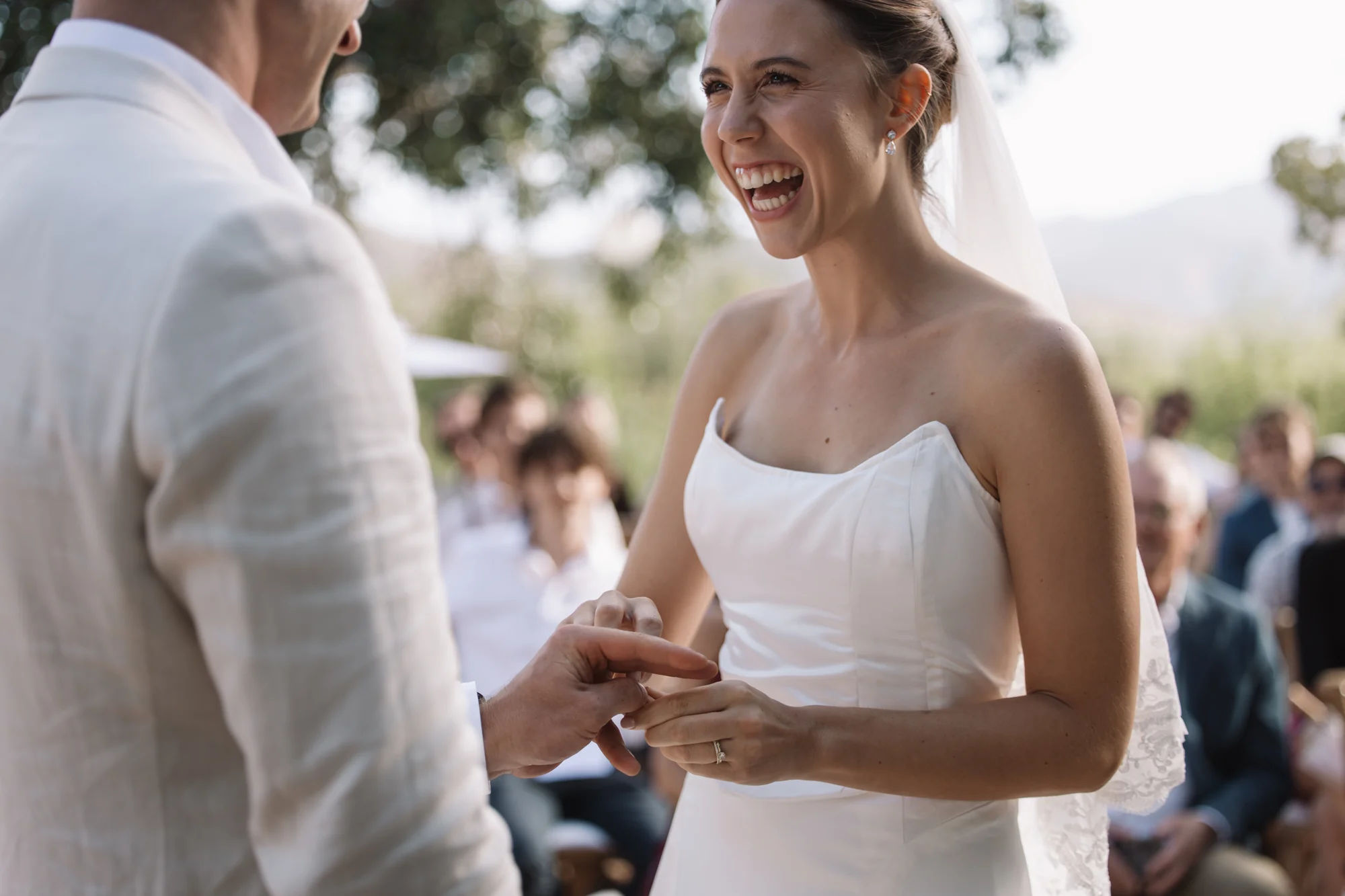 A bride laughing as the groom places a ring on her finger.