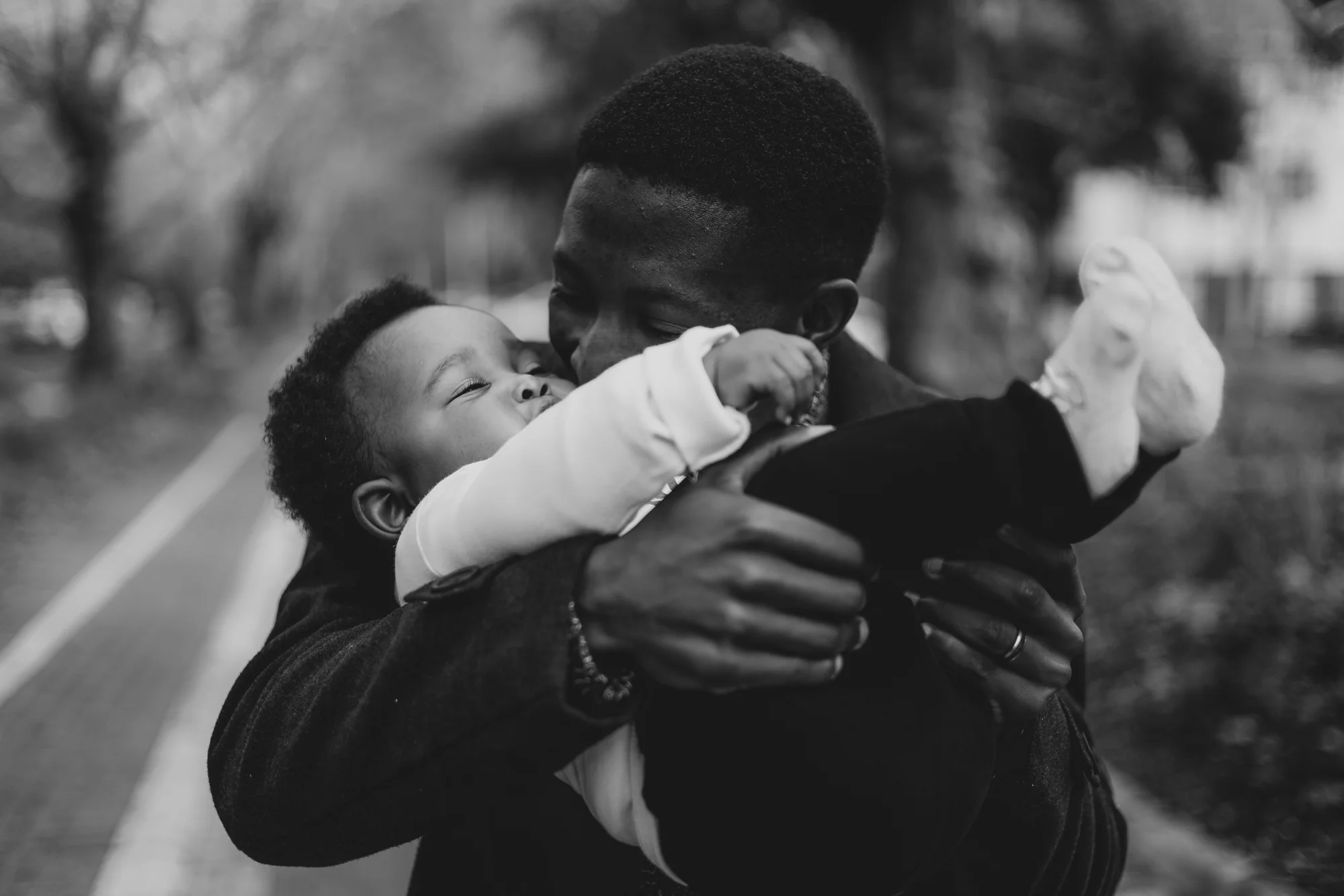Godfrey Mmagawo kisses his baby son on the cheek, in black and white.