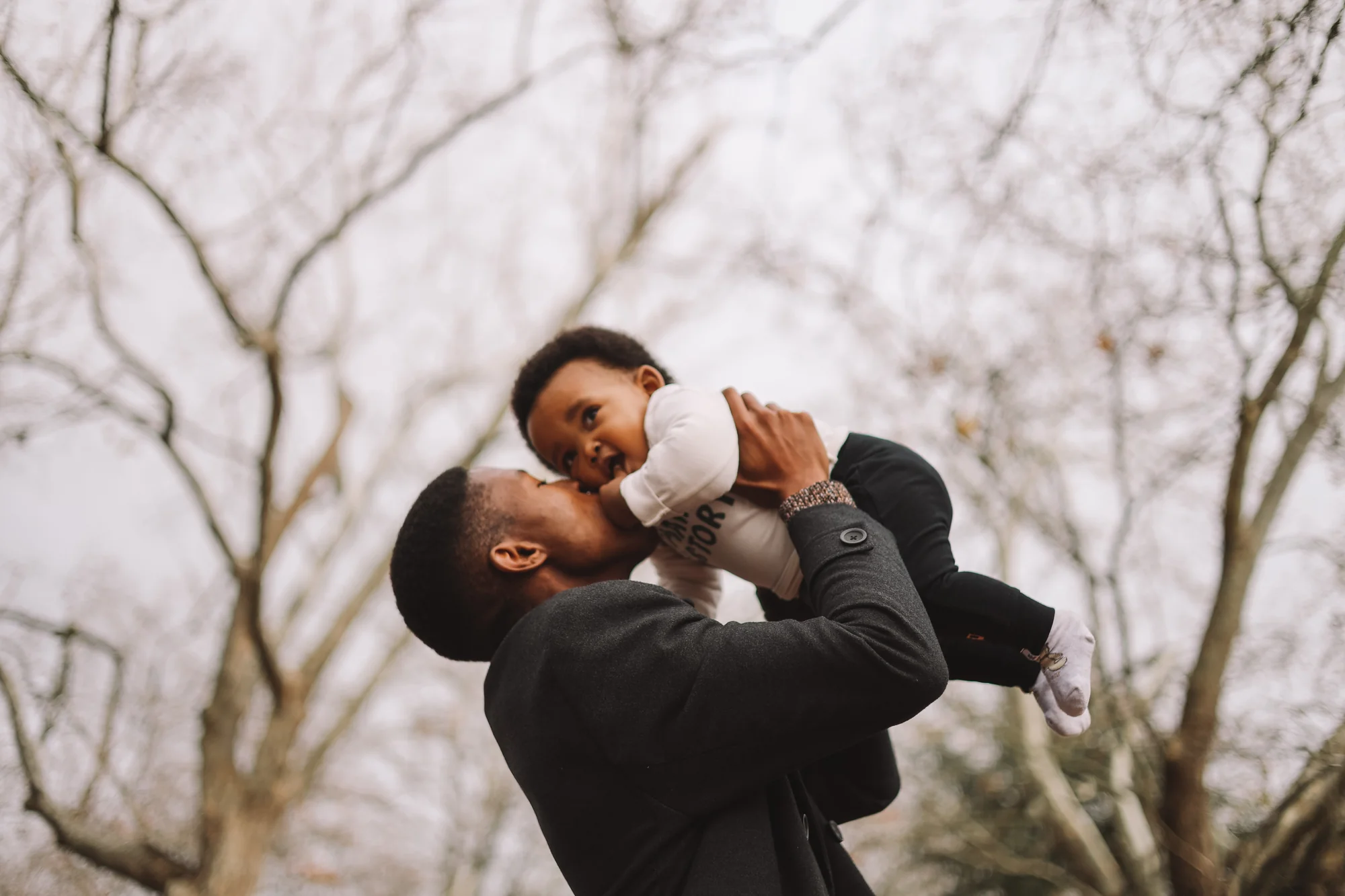 Godfrey Mmagawo lifts his son up under bare winter trees, both smiling.